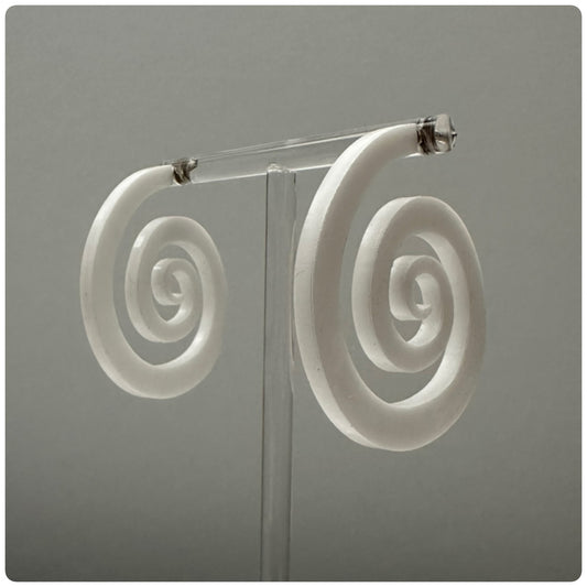 Striking lucite spiral hoop earrings. The spiral represents growth and evolution. The spiral’s outward movement signifies the idea of progress and forward motion. It encourages us to embrace change and continue growing, even when faced with challenges or obstacles.&nbsp;Meticulously handcrafted in the USA, these unique statement pieces feature sterling silver posts and are available in three stunning colors: Smokey grey, opaque white, and neon pink.